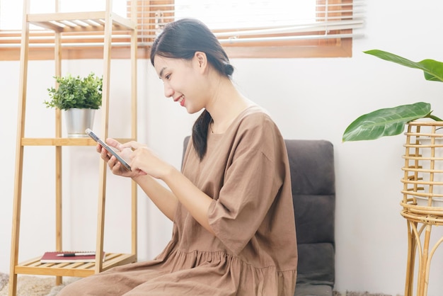 Concept de style de vie de relaxation Une jeune femme asiatique utilise un smartphone pour surfer sur les réseaux sociaux dans le salon