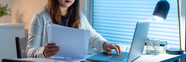 Concept de surmenage La femme qui fait son travail tard dans la nuit en lisant des papiers et en les tapant sur le cahier.