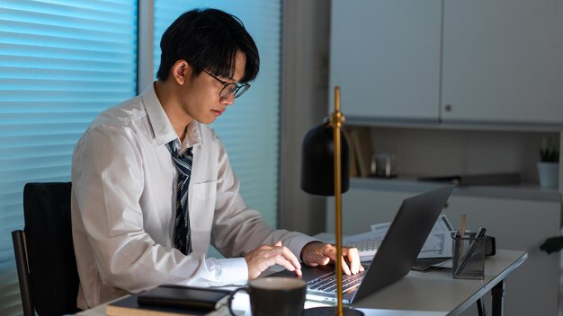 Concept de surmenage L'homme assis à son bureau et se concentrant sur le travail à travers son ordinateur portable