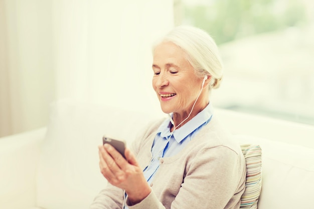 concept de technologie, d'âge et de personnes - femme senior heureuse avec smartphone et écouteurs écoutant de la musique à la maison