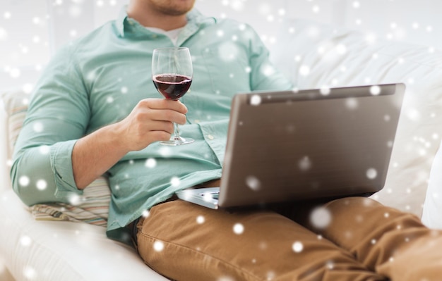 concept de technologie, de boissons, de loisirs, de maison et de style de vie - gros plan d'un homme avec un ordinateur portable et un verre de vin à la maison