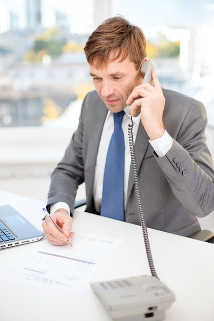 Photo concept de technologie, d'entreprise, d'internet et de bureau - bel homme d'affaires travaillant avec un ordinateur portable, un téléphone et des documents