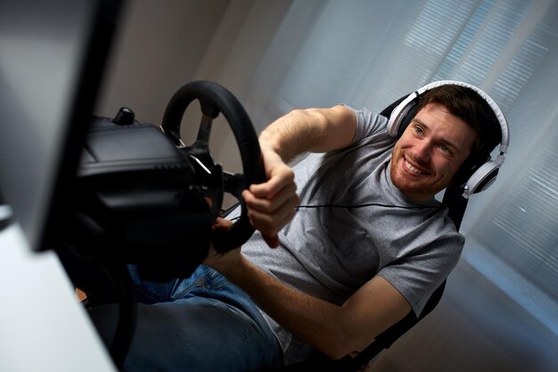 concept de technologie, de jeu, de divertissement et de personnes - heureux jeune homme souriant dans des écouteurs avec un ordinateur pc jouant à un jeu vidéo de course automobile à la maison et au volant
