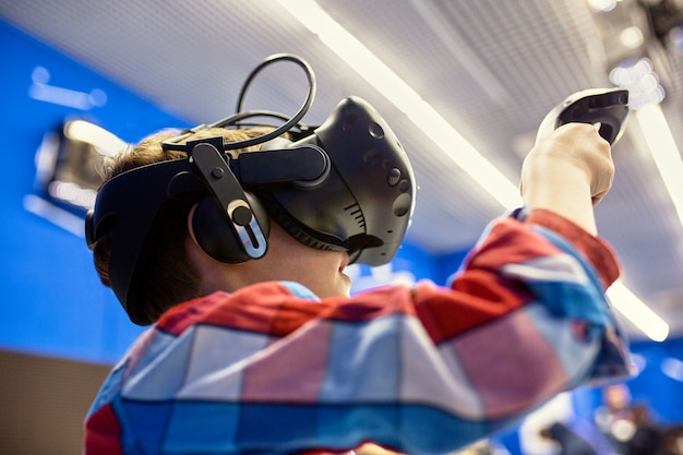 Concept de technologie, de jeu et de personnes modernes - garçon dans un casque de réalité virtuelle ou des lunettes 3D jouant au jeu vidéo au Game Center
