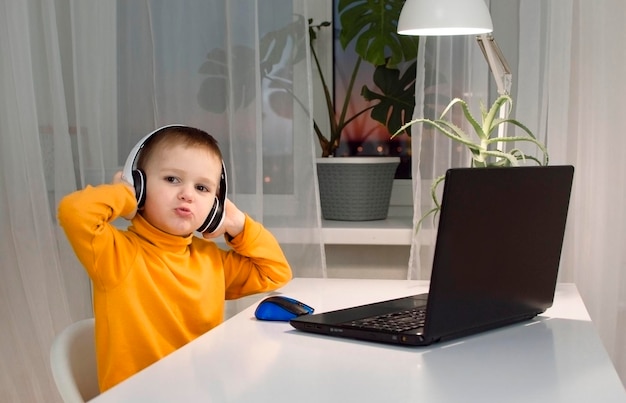 Concept de technologie, de jeux et de personnes - un garçon avec des écouteurs jouant à un jeu vidéo sur un ordinateur à la maison le soir. Le concept de développement de l'enfant, de l'enfance, de la communication en ligne.