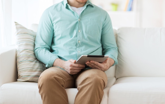 concept de technologie, de loisirs, de style de vie et d'apprentissage à distance - gros plan d'un homme travaillant avec un ordinateur tablette assis sur un canapé à la maison