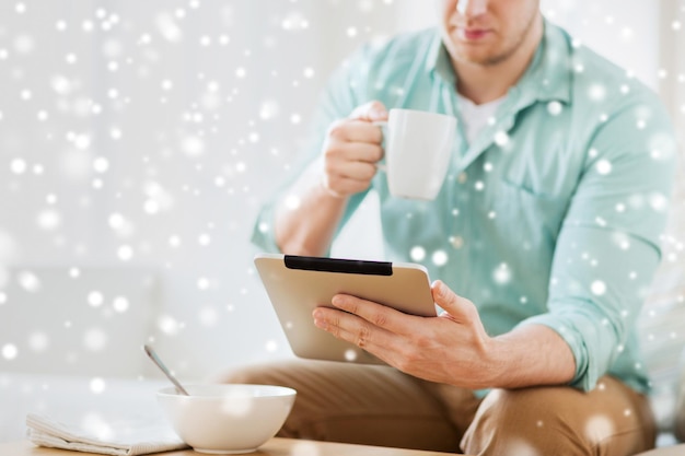 concept de technologie, de maison, de boissons, de nourriture et de style de vie - gros plan d'un homme avec un ordinateur tablette et une tasse prenant son petit déjeuner à la maison