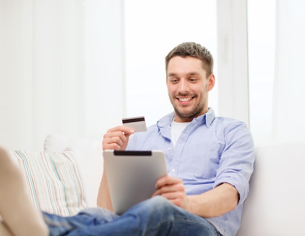 concept de technologie, de maison et de style de vie - homme souriant travaillant avec un ordinateur tablette et une carte de crédit à la maison