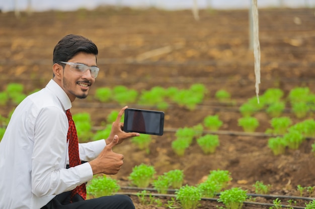 Concept de technologie et de personnes, jeune agronome indien utilisant une tablette ou un smartphone à effet de serre