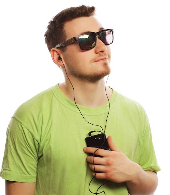 Concept de technologie et de personnes - jeune homme portant un t-shirt vert écoutant de la musique et utilisant un smartphone, isolé sur blanc