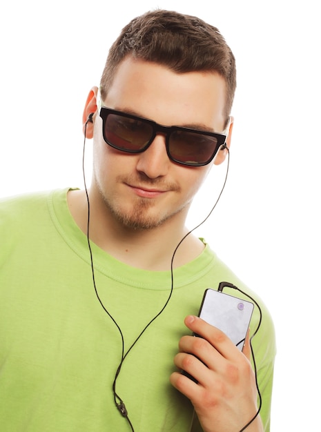 Concept de technologie et de personnes - jeune homme portant un t-shirt vert écoutant de la musique et utilisant un smartphone, isolé sur blanc