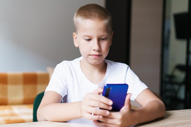 Concept de technologie et de personnes de loisirs pour enfants garçon souriant avec smartphone assis à table écoutant t...