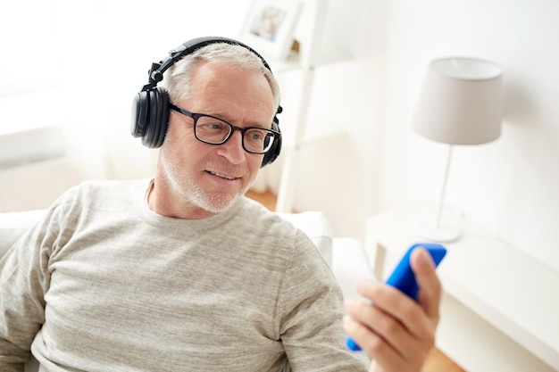 concept de technologie, de personnes, de style de vie et d'apprentissage à distance - homme senior heureux avec smartphone et écouteurs écoutant de la musique à la maison