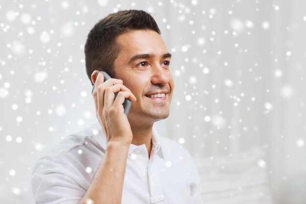 concept de technologie, de personnes, de style de vie et de communication - homme heureux appelant sur smartphone à la maison sur l'effet de neige