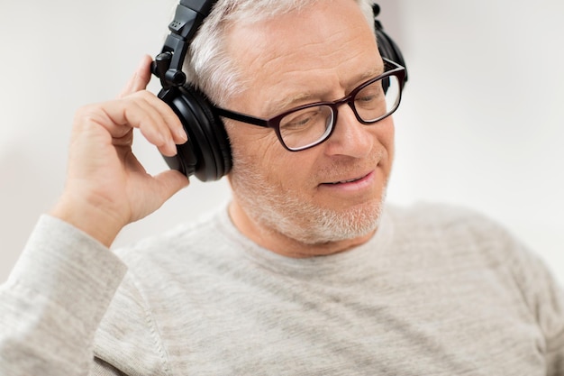 concept de technologie, de personnes et de style de vie - gros plan d'un homme âgé heureux dans des écouteurs écoutant de la musique à la maison