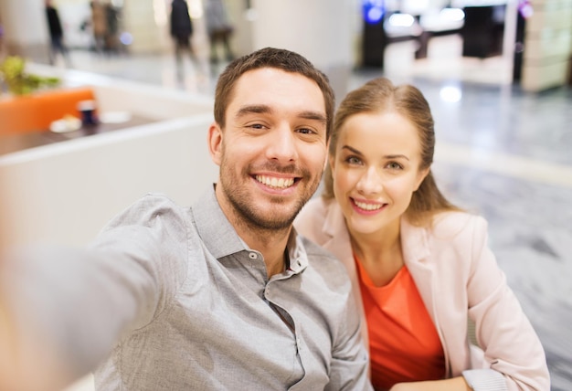 concept de technologie, de photographie et de personnes - couple heureux prenant un selfie avec un smartphone ou un appareil photo dans un centre commercial