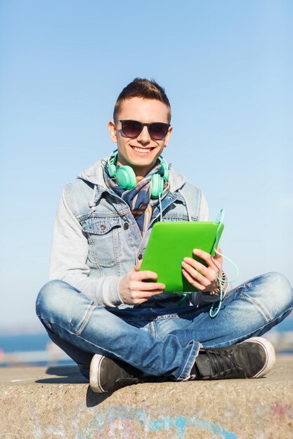 concept de technologie, de style de vie, de musique et de personnes - jeune homme ou adolescent souriant avec ordinateur tablette et casque à l'extérieur