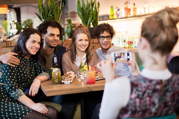 concept de technologie, de style de vie et de personnes - amis heureux avec smartphone photographiant au bar ou au café