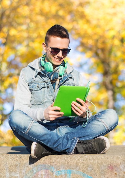 concept de technologie, de style de vie, de saison, de musique et de personnes - jeune homme souriant ou adolescent avec ordinateur tablette et casque sur fond de parc d'automne