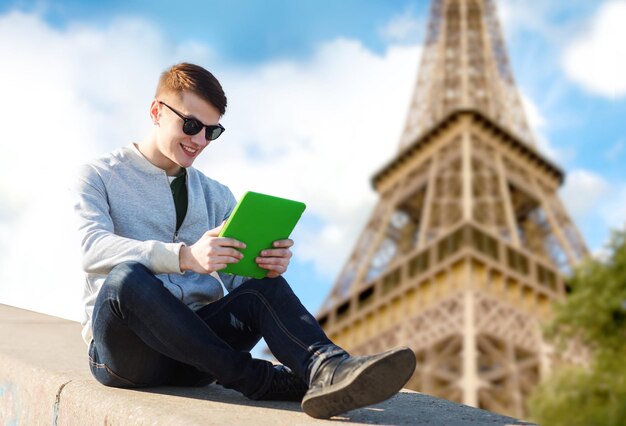 concept de technologie, de voyage, de tourisme et de personnes - jeune homme souriant ou adolescent avec des ordinateurs tablettes sur fond de tour eiffel de paris