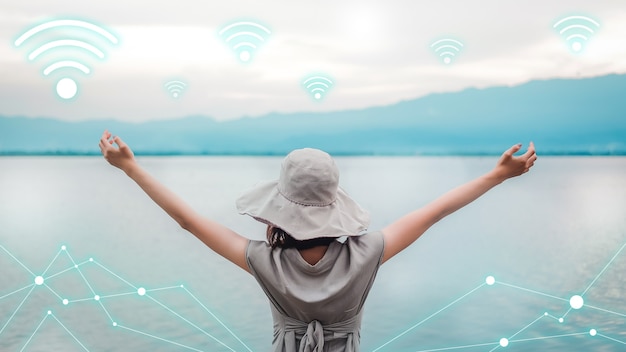 Concept de technologie wifi. Connexion réseau ou symbole de signal téléphonique avec jeune femme asiatique portant un chapeau et levant les bras tendus avec des lacs et des montagnes