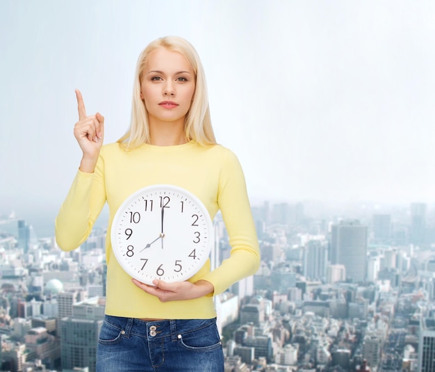 concept de temps, d'éducation et de personnes - jeune femme sérieuse avec horloge murale montrant 8 et doigt vers le haut