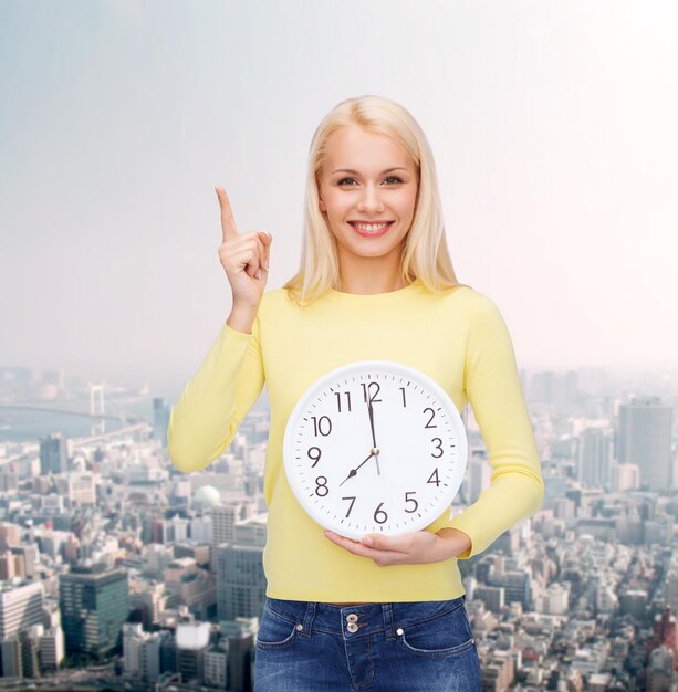 concept de temps, d'éducation et de personnes - jeune femme souriante avec horloge murale montrant 8 et doigt vers le haut