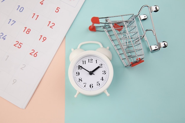 Concept de temps de magasinage. Chariot de supermarché avec réveil et calendrier.