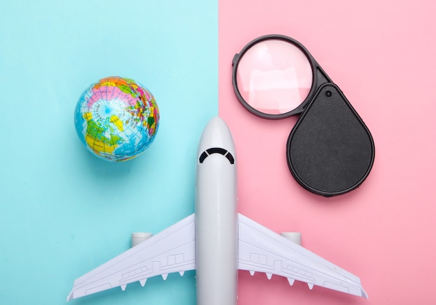 Concept de tourisme et de voyage. Globe, loupe et figurine d'avion de passagers sur le mur pastel bleu rose Vue de dessus. Mise à plat