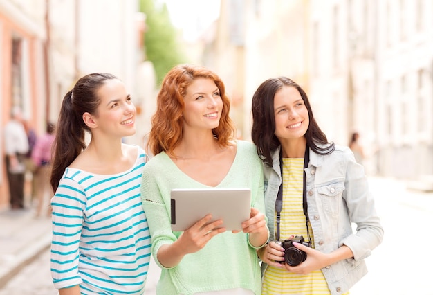 concept de tourisme, de voyage, de loisirs, de vacances et d'amitié - adolescentes souriantes avec ordinateur tablette sorcière et appareil photo à l'extérieur