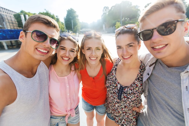 concept de tourisme, de voyage, de personnes, de loisirs et de technologie - groupe d'amis adolescents souriants prenant un selfie à l'extérieur