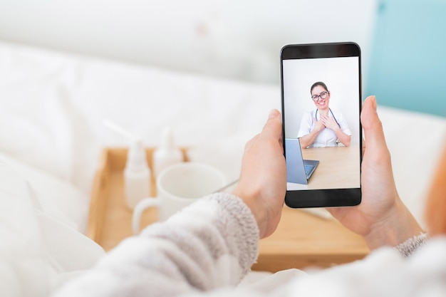 Le concept de traitement à distance Vue arrière d'une femme au lit en pyjama avec un smartphone dans les mains Un patient grippé regarde un blog vidéo médical