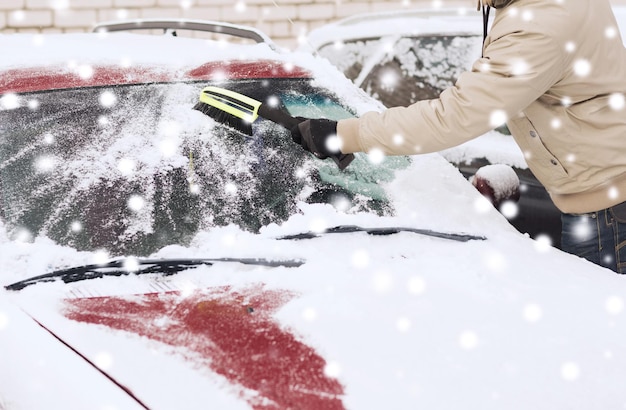 concept de transport, d'hiver, de personnes et de véhicules - gros plan d'un homme nettoyant la neige du pare-brise de voiture avec une brosse