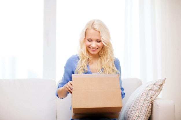 concept de transport, de poste et de personnes - jeune femme souriante ouvrant une boîte en carton à la maison