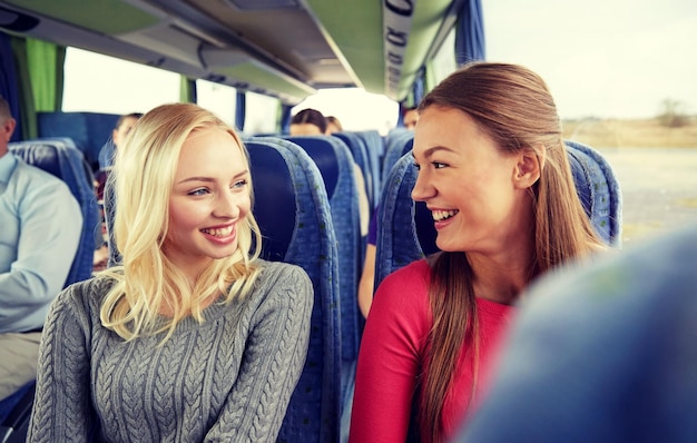 concept de transport, de tourisme, d'amitié, de voyage sur la route et de personnes - jeunes femmes heureuses assises et en conversation dans un bus de voyage
