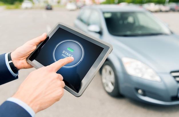 concept de transport, de voyage d'affaires, de technologie et de personnes - gros plan de mains masculines appuyant sur le bouton de démarrage du moteur sur l'écran de l'ordinateur tablette pc avec voiture à l'extérieur