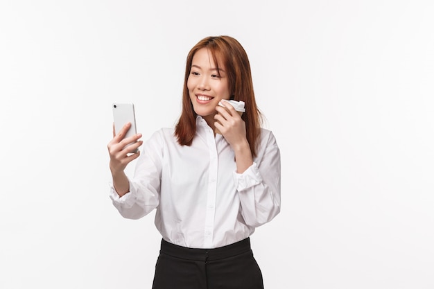 Concept de travail de bureau, de personnes et de style de vie. Portrait d'élégante et jolie jeune femme asiatique prenant selfie, enregistrer une vidéo pour publier les médias sociaux, en utilisant le filtre d'application pour photo avec du café à emporter, souriant