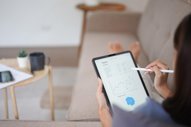 Concept de travail à domicile Les femmes d'affaires lisent des données financières sur une tablette en position allongée sur un canapé à la maison