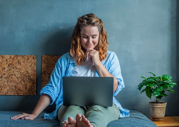 concept de travail à domicile travailleur à distance indépendant fille assise sur le lit avec un ordinateur portable et travaillant en souriant