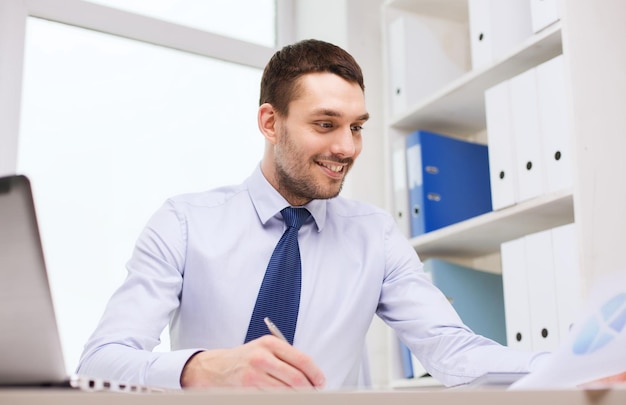 concept de travail d'entreprise, de personnes et de papier - homme d'affaires souriant avec ordinateur portable et papiers écrits au bureau