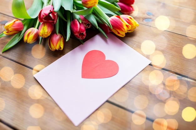 concept de vacances, d'amour et de saint valentin - gros plan de fleurs de tulipes et carte de voeux avec coeur sur table en bois