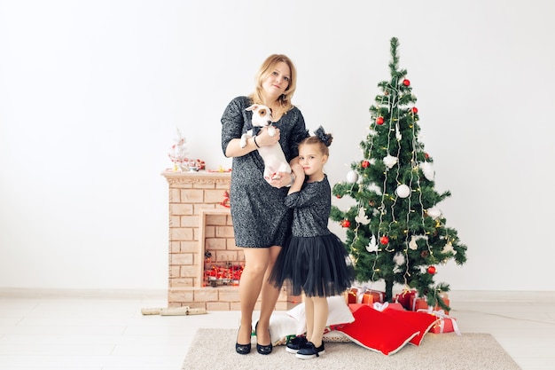 Concept de vacances et d'animaux de compagnie - mère et fille jouant avec un chien jack russell terrier devant l'arbre de noël à la maison.