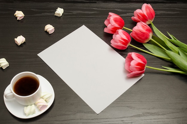 Concept de vacances. Bouquet de tulipes roses, une tasse de café, de guimauve et une feuille de papier sur un fond en bois noir