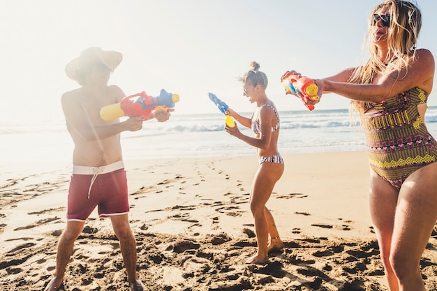 Concept de vacances d'été amusant avec un groupe de jeunes amis caucasiens jouant avec un pistolet à eau à la plage sur le sable avec une scène d'océan et de ciel