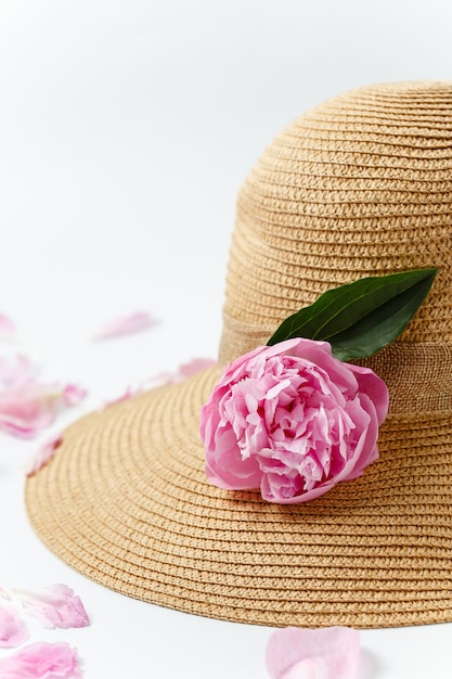 Concept de vacances d'été, chapeau tressé de paille, fleurs de pivoine rose et pétales sur une surface blanche, vue de dessus. Bannière de vacances et de voyage.