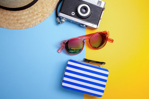 Concept de vacances d'été, concept de voyage avec sac, appareil photo et chapeau sur fond bleu et jaune. Mise à plat