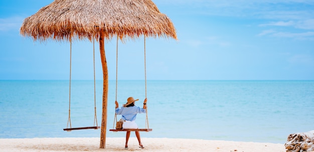 Concept de vacances d'été Jeune femme vêtue d'une élégante robe bleue et chapeau de paille avec un ciel bleu sur la plage.