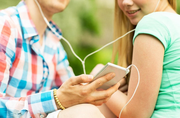 concept de vacances d'été, de technologie et de personnes - gros plan d'un couple souriant avec smartphone et écouteurs écoutant de la musique dans le parc