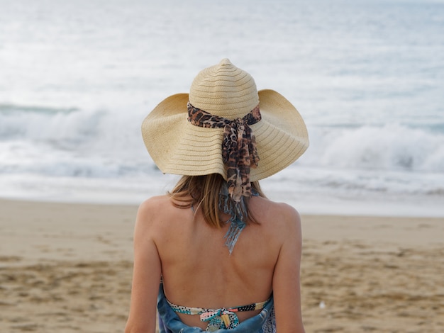 Concept de vacances d'été, vacances, voyages et personnes. Femme au chapeau de soleil sur la plage sur l'océan et le ciel bleu. Vue arrière.