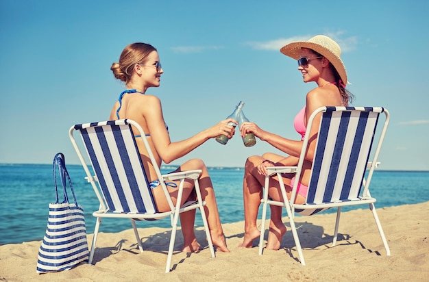 concept de vacances d'été, de voyage et de personnes - femmes heureuses buvant de la bière et prenant un bain de soleil dans des salons sur la plage